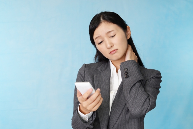 スマートフォンを見ながら首の横を押さえる女性